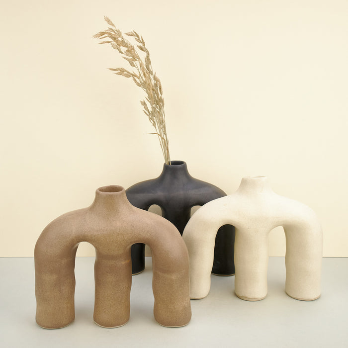 two sculptural ceramic vases, in black, beige and white across a plain background. 