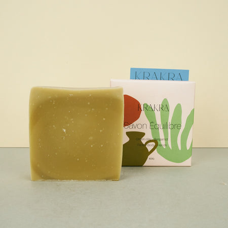 green soap next to soap covered in colourful box on plain background. 
