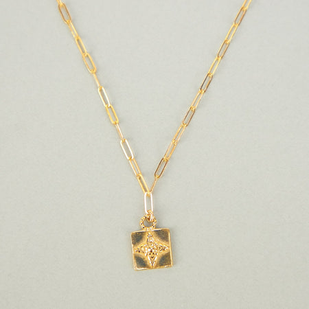gold necklace with square pendant on plain background