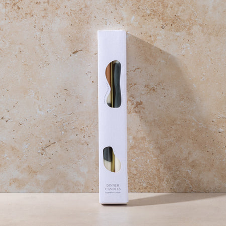 White candle packaging with black and camel design on a beige stone background