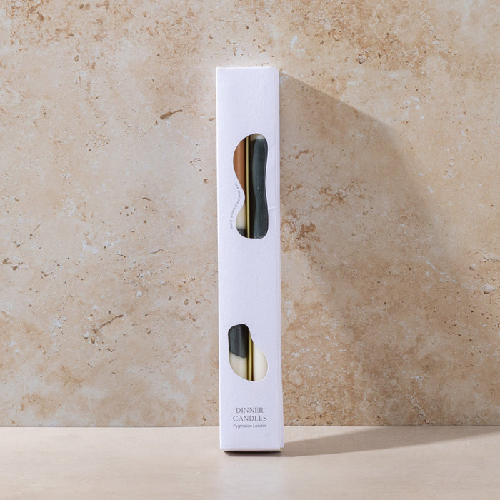 White candle packaging with black and camel design on a beige stone background