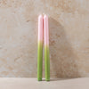 Two gradient candles, ombre pink to green on a beige stone background.