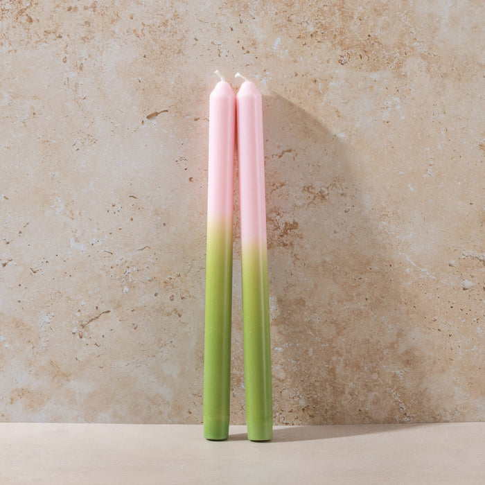Two gradient candles, ombre pink to green on a beige stone background.