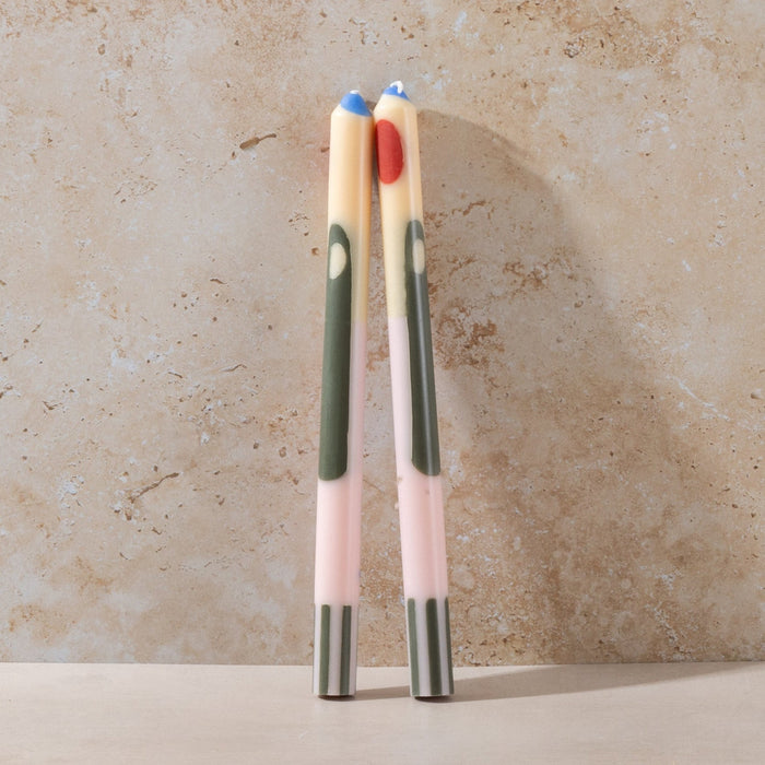 Two colourful abstract candles with gradient designs on a beige stone background