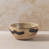 Ceramic bowl with black abstract design on a beige surface and textured wall background