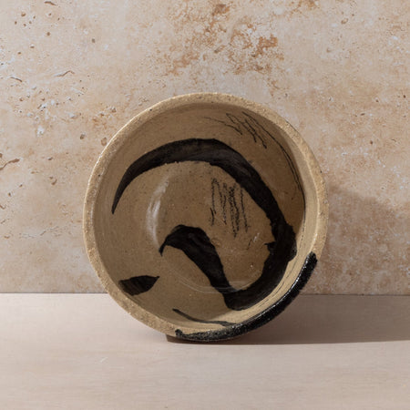 Ceramic bowl with black abstract design on a beige stone surface