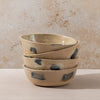 Stack of ceramic bowls with speckled design on a beige surface and background