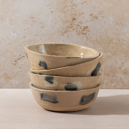 Stack of ceramic bowls with speckled design on a beige surface and background