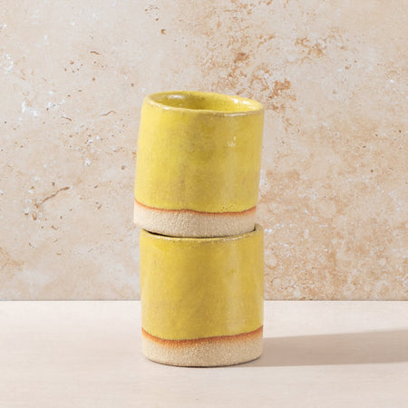 Two stacked ceramic cups with a yellow glaze on a beige background