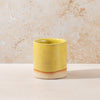 Yellow ceramic cup on a beige surface with a textured beige wall background