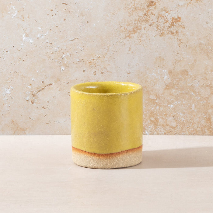 Yellow ceramic cup on a beige surface with a textured beige wall background