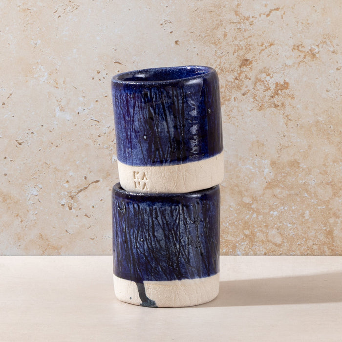 Two blue ceramic cups stacked on a beige surface with a textured wall background
