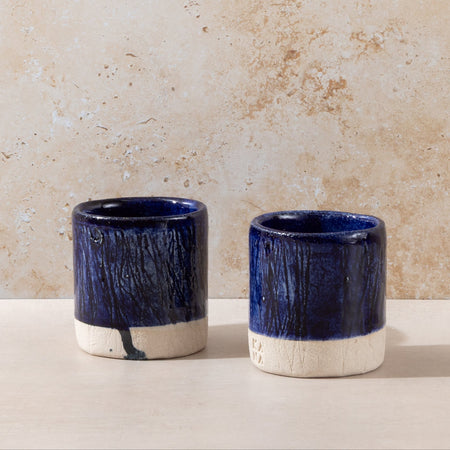 Two blue ceramic cups with white bases on a beige surface and background