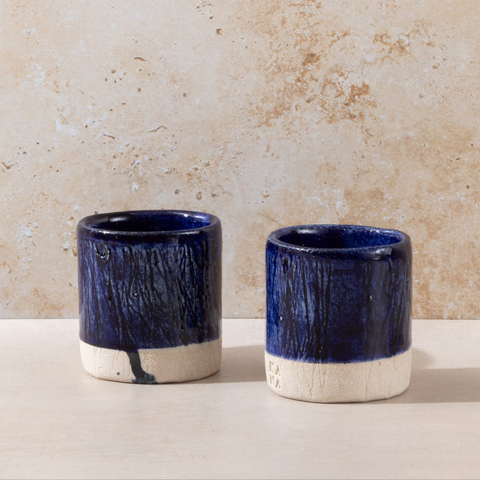 Two blue ceramic cups with white bases on a beige surface and background