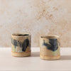 Two ceramic cups with black and green accents on a beige surface and background