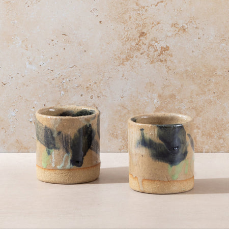 Two ceramic cups with black and green accents on a beige surface and background