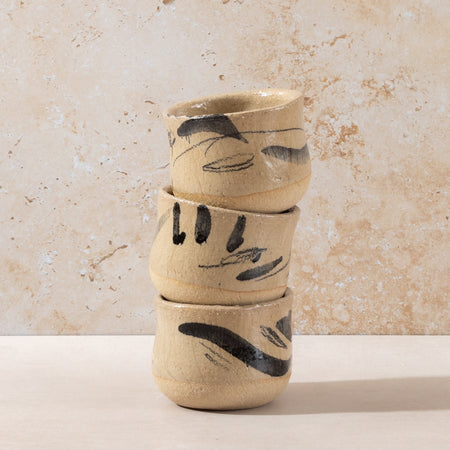 Stack of three ceramic cups with black abstract designs on a beige background