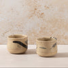 Two ceramic cups with feather designs on a beige surface and background