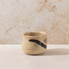 Small ceramic cup with black design on a beige surface and background