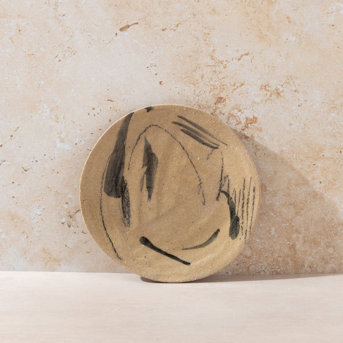 Round plate with black abstract design on a beige stone background
