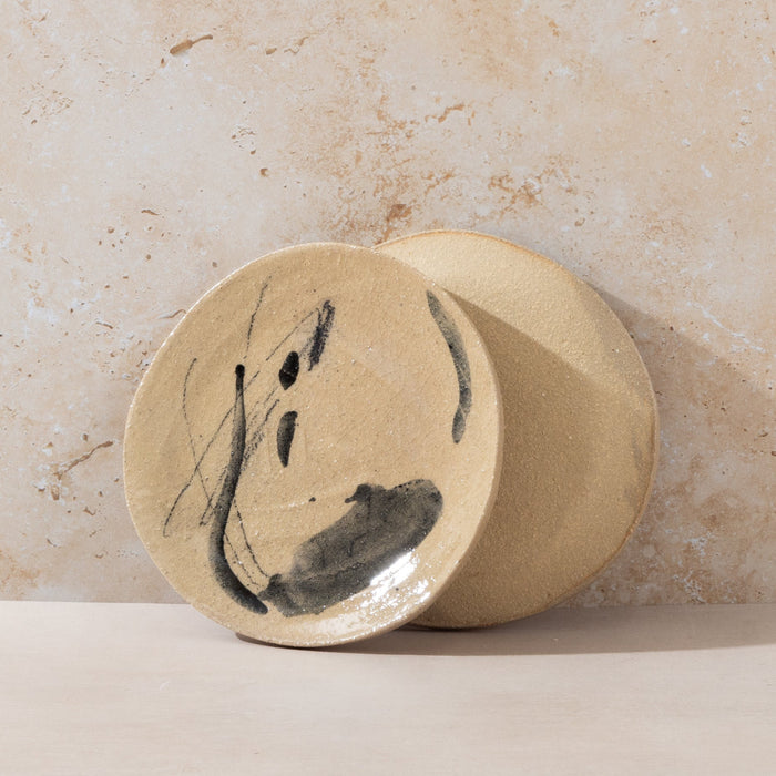 Two ceramic plates with artistic black designs on a beige stone background