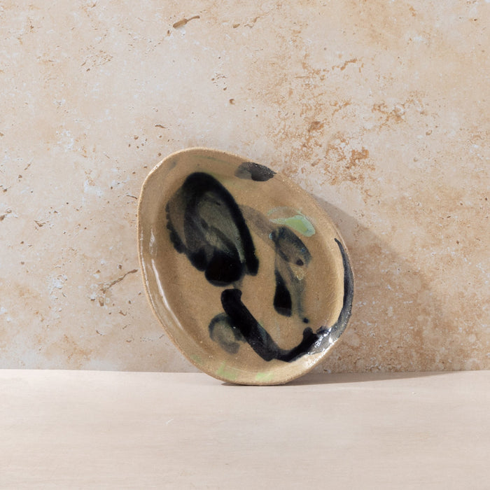 Ceramic plate with black and green abstract design on a beige background