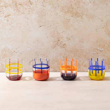 Four colorful glass tumblers on a light surface with a beige background