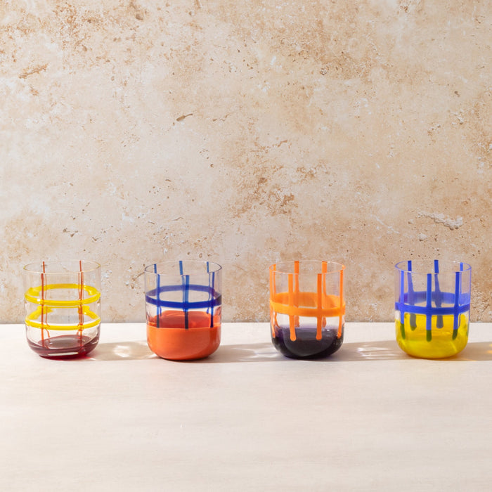 Four colorful glass tumblers on a light surface with a beige background