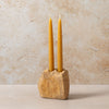 Two yellow candles in a stone holder against a beige background
