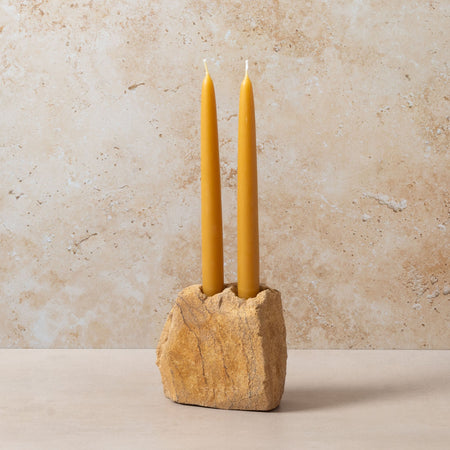 Two yellow candles in a stone holder against a beige background