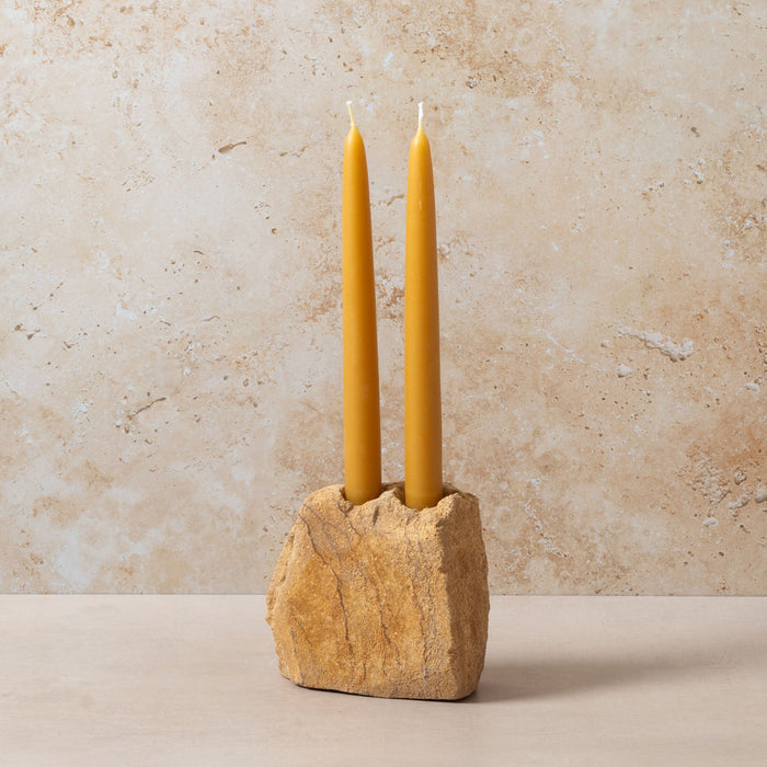Two yellow candles in a stone holder against a beige background