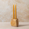 Two yellow candles in a stone holder against a beige background