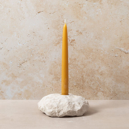 Yellow candle on a stone holder against a beige wall