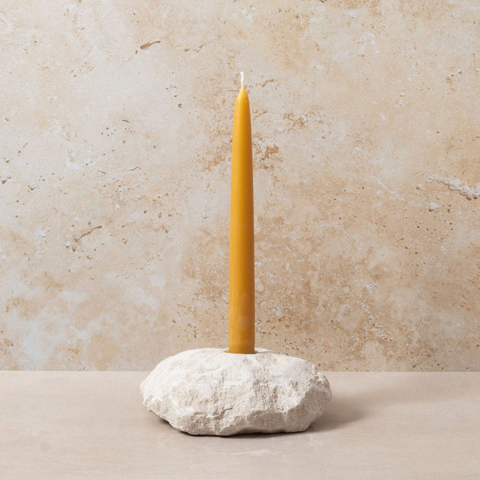 Yellow candle on a stone holder against a beige wall