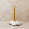 Yellow candle in a stone holder against a beige wall