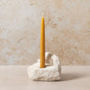 Yellow candle in a stone holder against a beige stone wall.