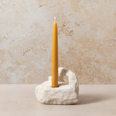 Yellow candle in a stone holder against a beige stone wall.