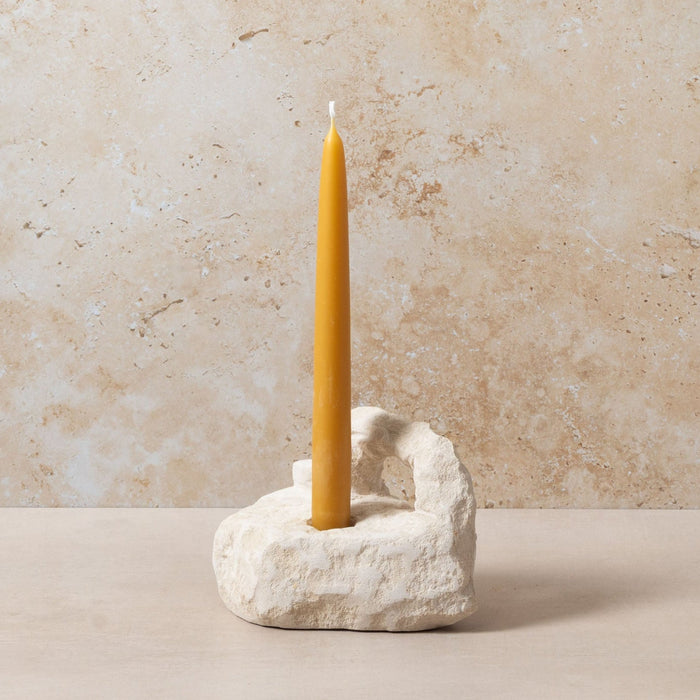 Yellow candle in a stone holder against a beige stone wall.