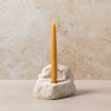 Yellow candle in a stone holder against a beige marble background