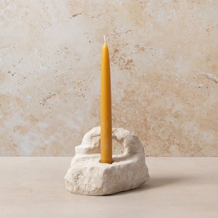 Yellow candle in a stone holder against a beige marble background