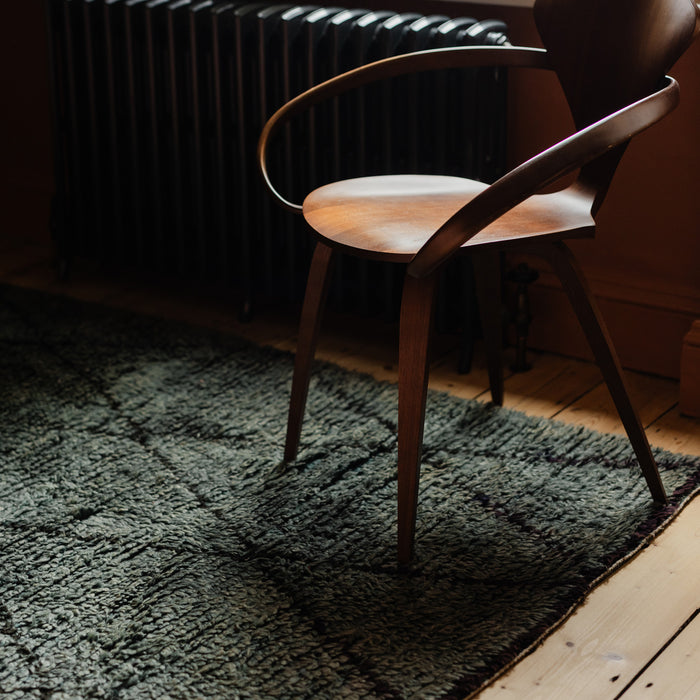 Moroccan Berber rug with black diamond pattern on blue / grey base in a modern boho rustic earthy interior, on a wooden floor.