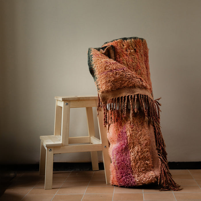 Moroccan Boujad wool hand-knotted rug with soft pink ombre base rolled and leaning against stool. Natural earthy interior tones and terracotta tiles