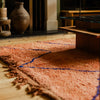 Rust-coloured peachy pink Moroccan Berber rug with a simple linear design in cobalt blue in an interior setting on a wooden floor.