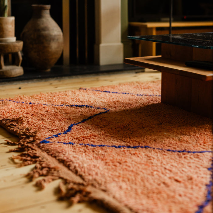 Rust-coloured peachy pink Moroccan Berber rug with a simple linear design in cobalt blue in an interior setting on a wooden floor.