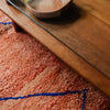 Rust-coloured peachy pink Moroccan Berber rug with a simple linear design in cobalt blue, placed under a coffee table.