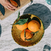 Person cutting oranges on a wooden board with a bowl of oranges nearby.