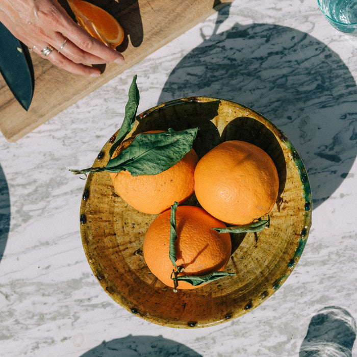 Person cutting oranges on a wooden board with a bowl of oranges nearby.