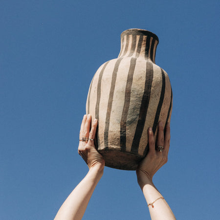 Person holding a striped ceramic vase against a clear blue sky