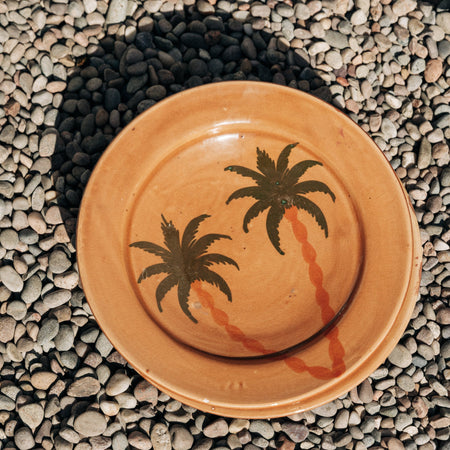 Ceramic plate with palm tree design on a pebbled surface