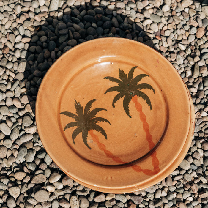 Ceramic plate with palm tree design on a pebbled surface